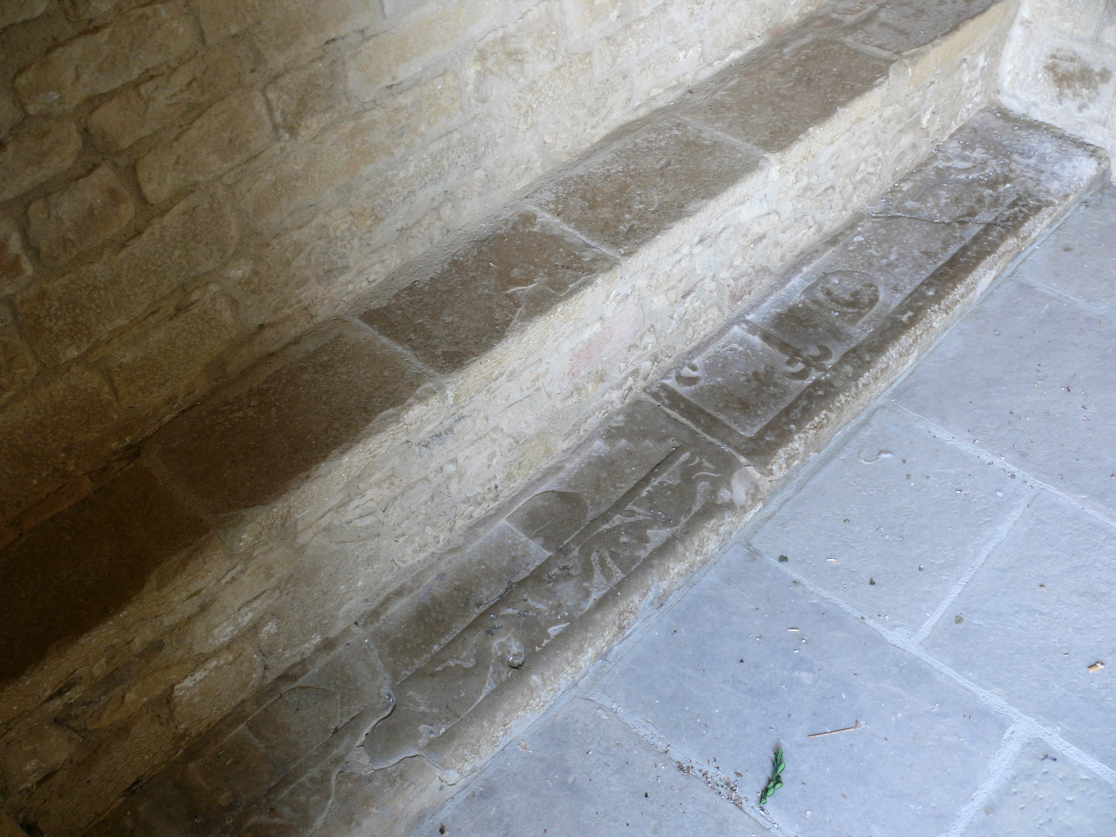 Dos laudas sepulcrales en el lateral izquierdo del pórtico, semiocultas por un banco de piedra.